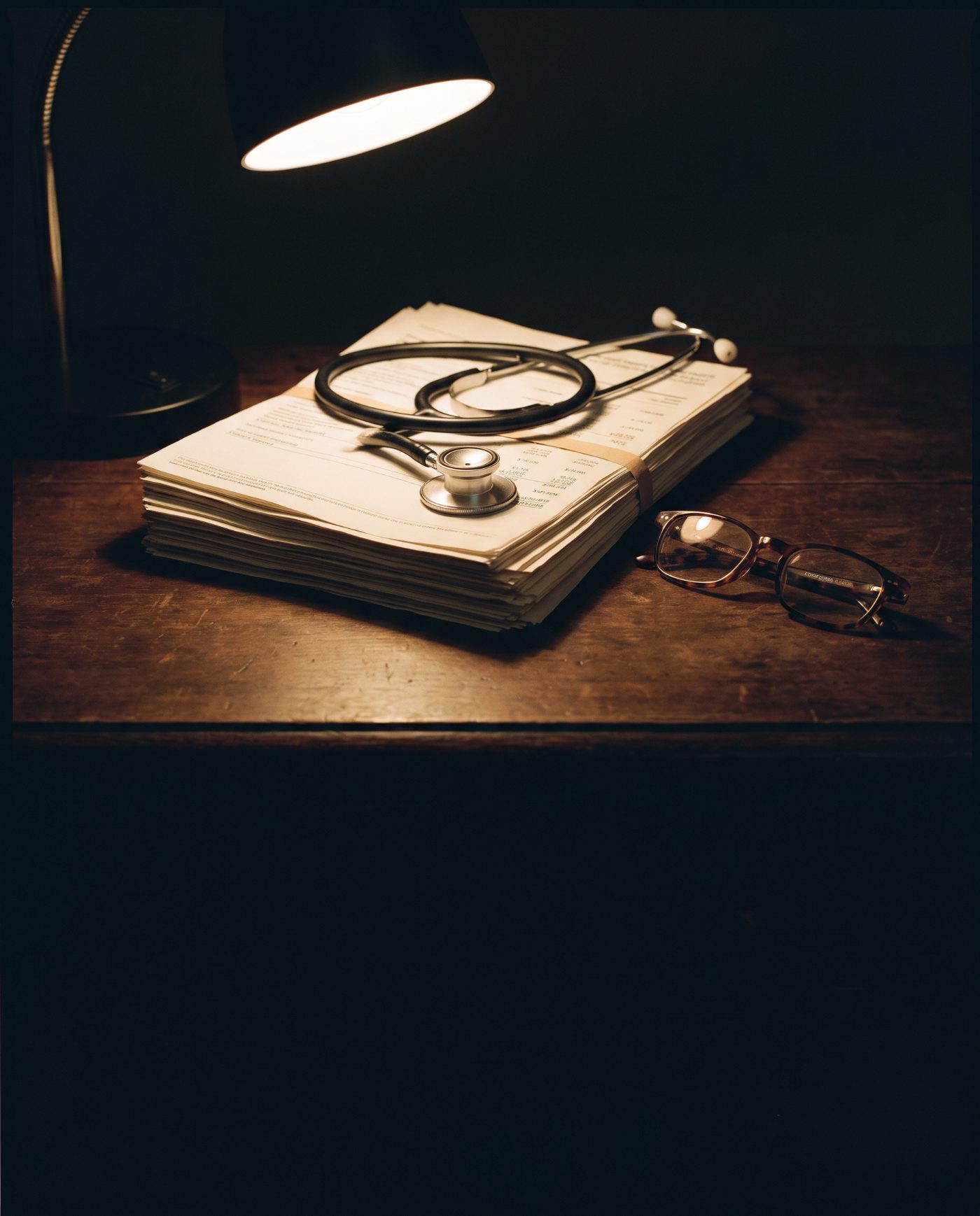 A stethoscope resting on a stack of retirement statements under a desk lamp